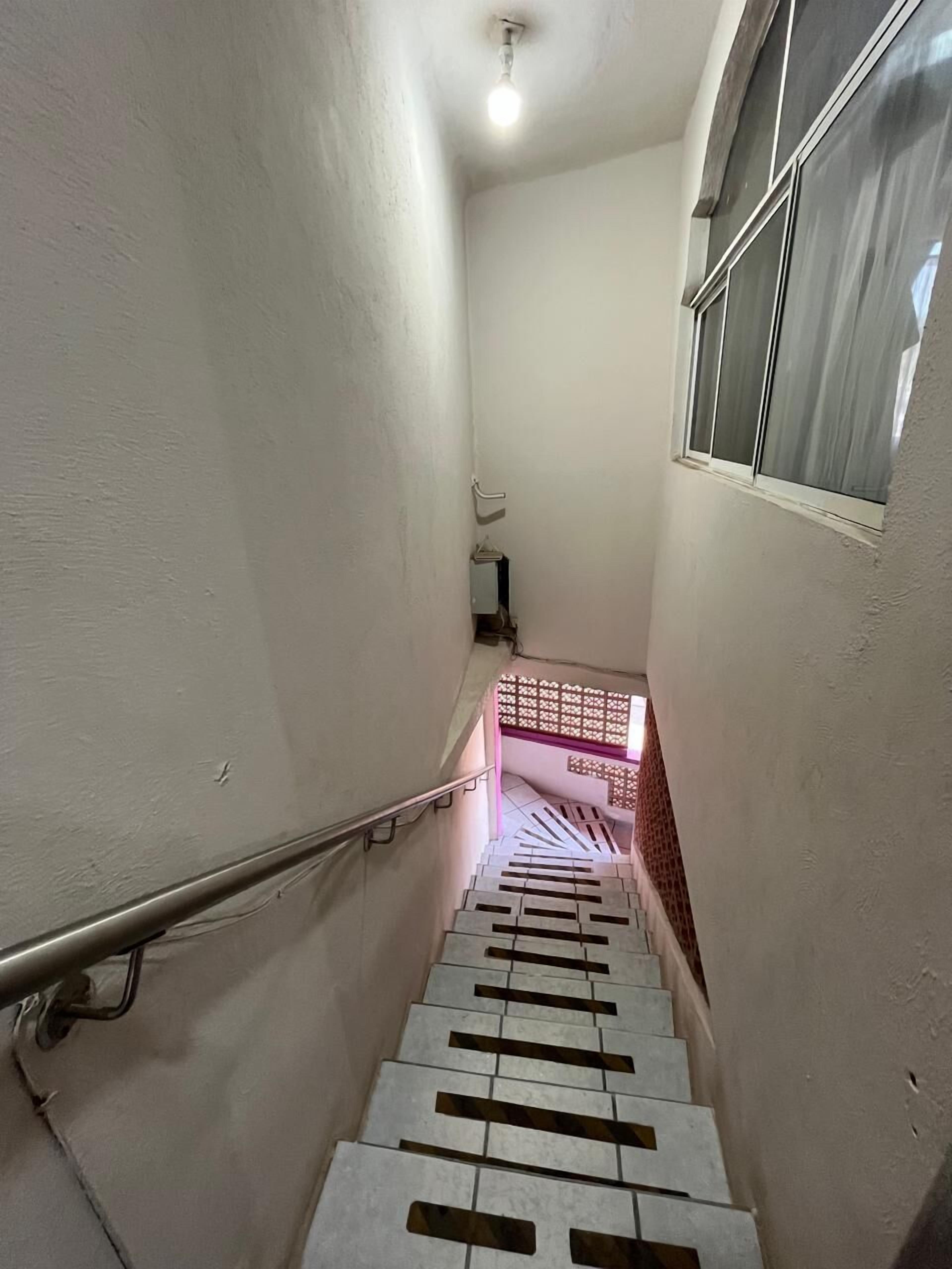 Eine enge Treppe mit Metallgeländer, einem Fenster mit Vorhang und einer Deckenleuchte.
