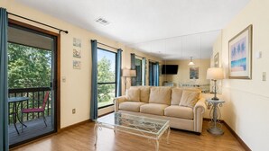 A living room with a sofa, a glass coffee table, a dining area with a table and chairs, and a balcony with a chair.