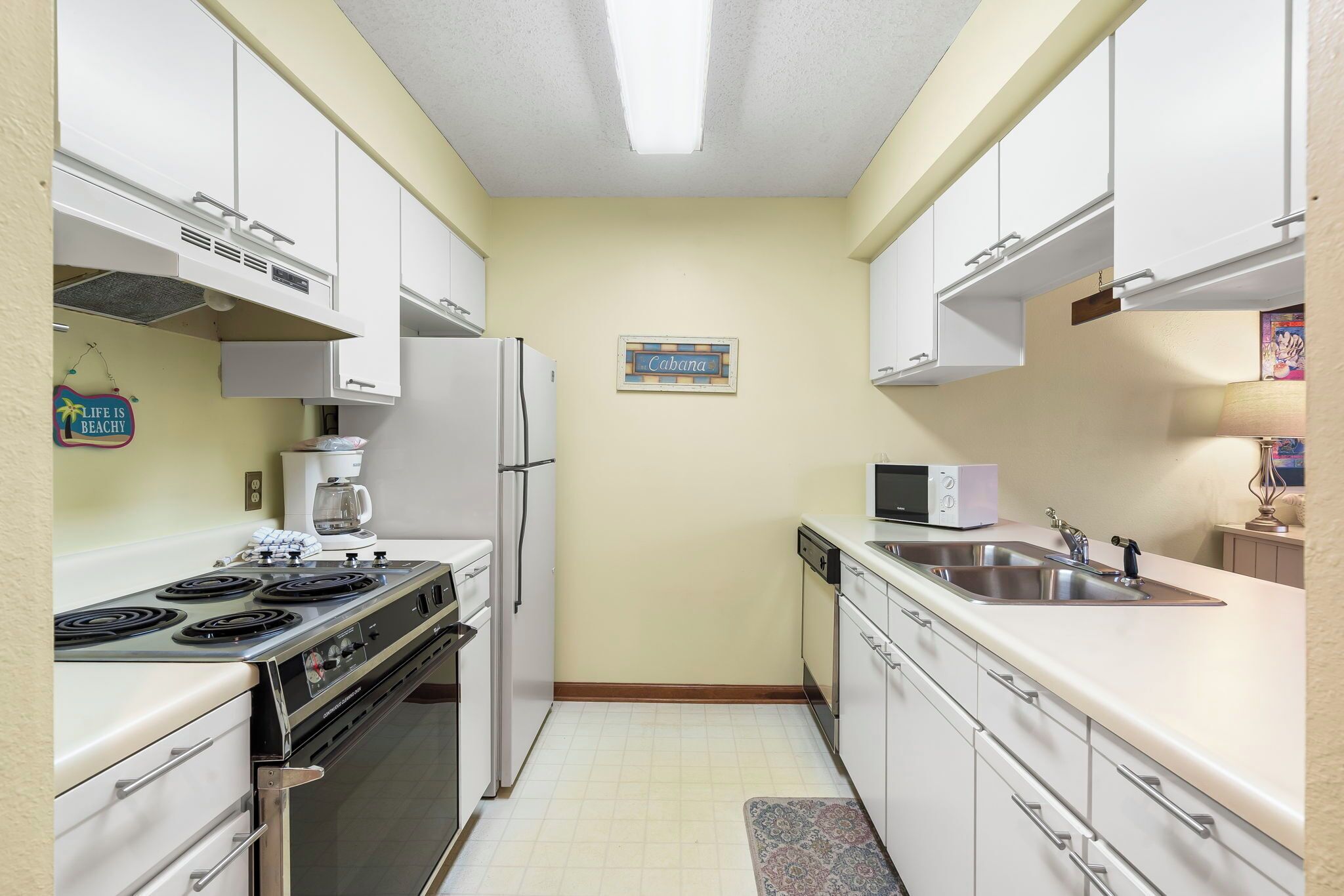 A compact kitchen with white cabinets, a stove, refrigerator, microwave, and a sink.