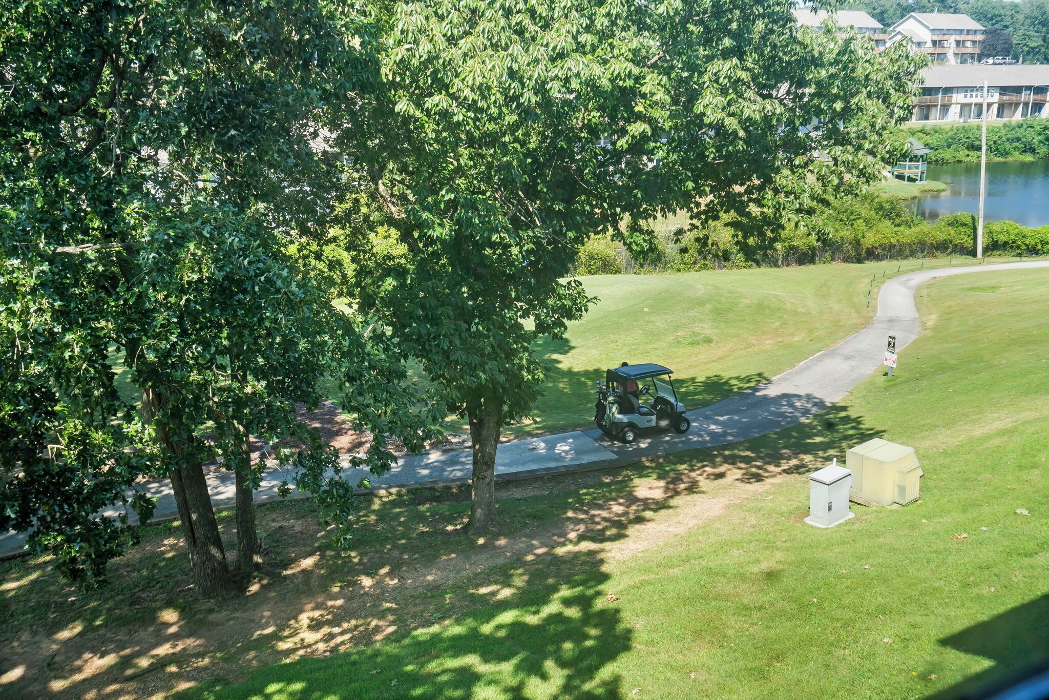 A golf course with a golf cart, trees, and a small building.