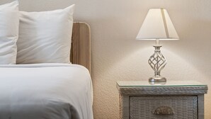Una cama bien hecha con sábanas blancas, una mesita de noche con lámpara y una pared con textura.