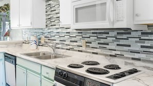 Una cocina con microondas, estufa y lavabo blancos.