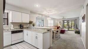 Une cuisine moderne avec des meubles blancs, un îlot central et un coin repas comprenant une chaise et une table rouges.