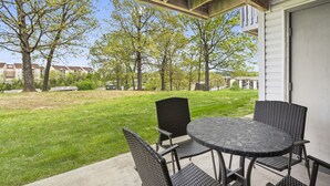 Una veranda esterna con un tavolo rotondo e sedie, una zona coperta con travi in legno, e vista su un quartiere residenziale con alberi e case.
