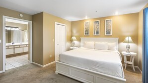 Una camera da letto con un letto grande, due comodini con lampade, una porta e uno specchio nel bagno vicino.