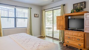 Ein Schlafzimmer mit einem Bett, einer Holzkommode, einem Fernseher und einer Glastür zu einer Terrasse.