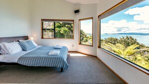 Une chambre à coucher avec un grand lit, deux fenêtres et une vue sur un paysage naturel.