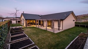 Une maison moderne dotée d’un grand patio, d’une pelouse bien entretenue et d’une cheminée en pierre.