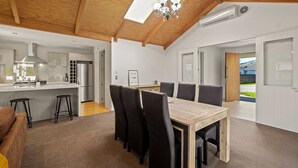 Une cuisine moderne dotée d’un îlot central, d’un coin repas avec une table en bois et des chaises noires, et d’une grande fenêtre offrant une vue sur l’extérieur.