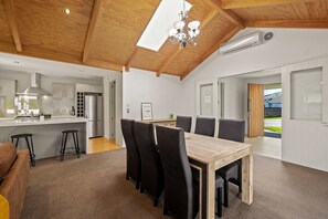 A modern kitchen with a central island, a dining area with a wooden table and black chairs, and a large window with a view of the outdoors. - Roys Bay Lodge - Wanaka Holiday Home (Wanaka)