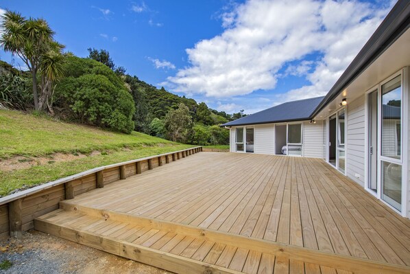 Eine Holzterrasse führt zu einem Haus mit großen Fenstern und einem dunklen Dach.
