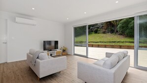 A modern living room with two grey sofas, a flat-screen TV on a wooden console, and large sliding glass doors leading to an outdoor deck.