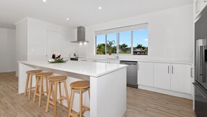 A modern kitchen with a large island, wooden stools, stainless steel appliances, and a view of greenery outside.
