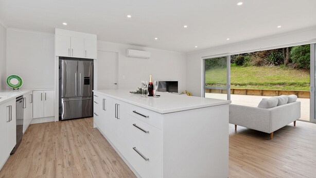 A modern kitchen with white cabinetry, a stainless steel refrigerator, and a dining area with a white table and grey sofa.