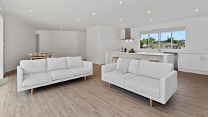 A modern living room with two white sofas, a dining area, and a kitchen with a view.