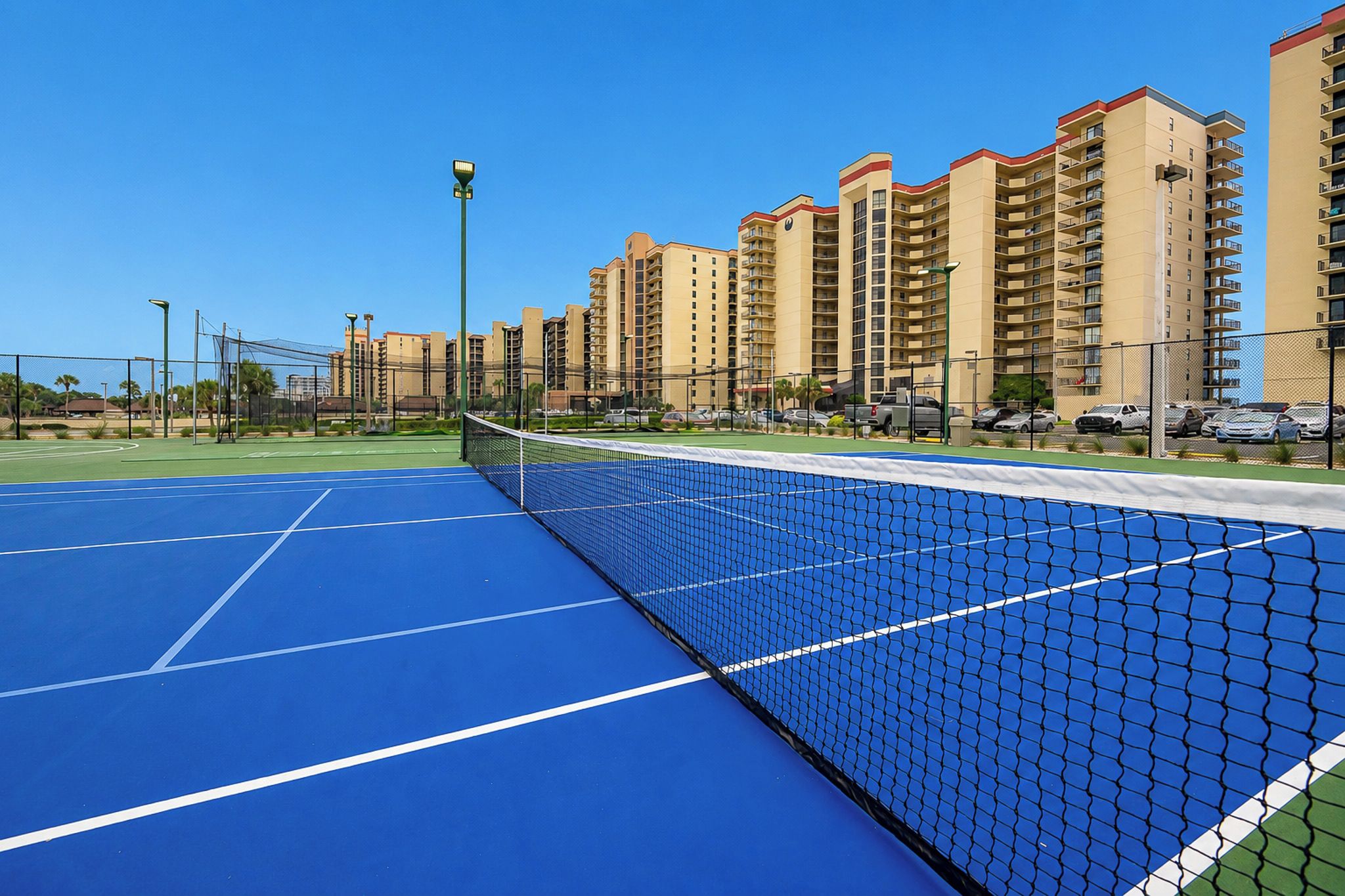 Un court de tennis en plein air, doté d’un filet, entouré d’immeubles d’habitation de grande hauteur.