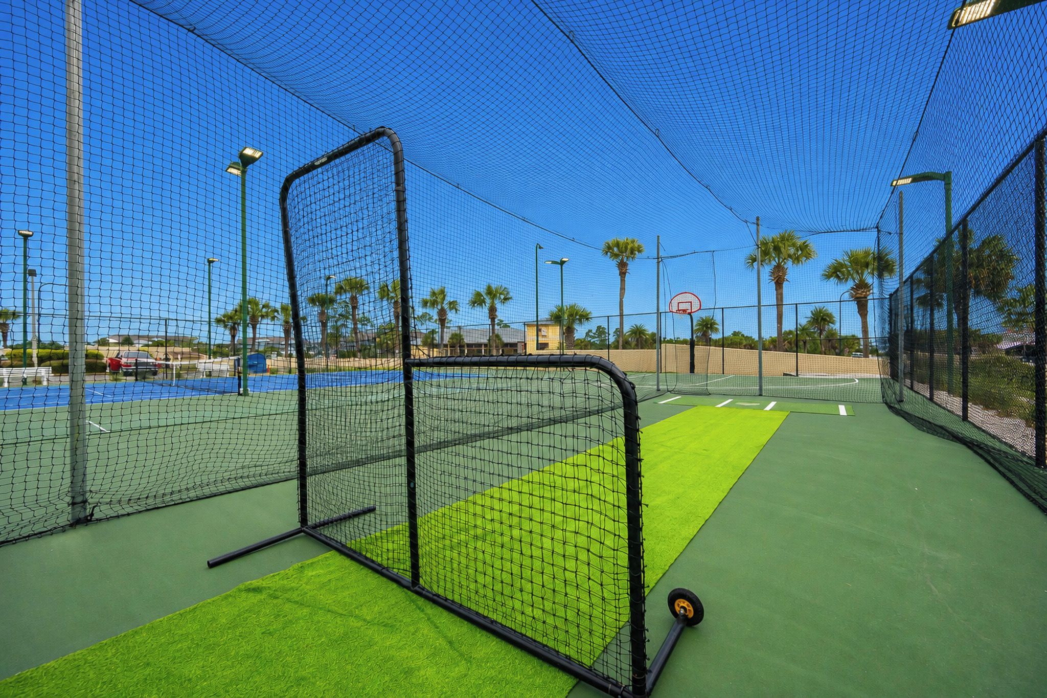 A tennis court with a net, green artificial turf, and a basketball hoop.