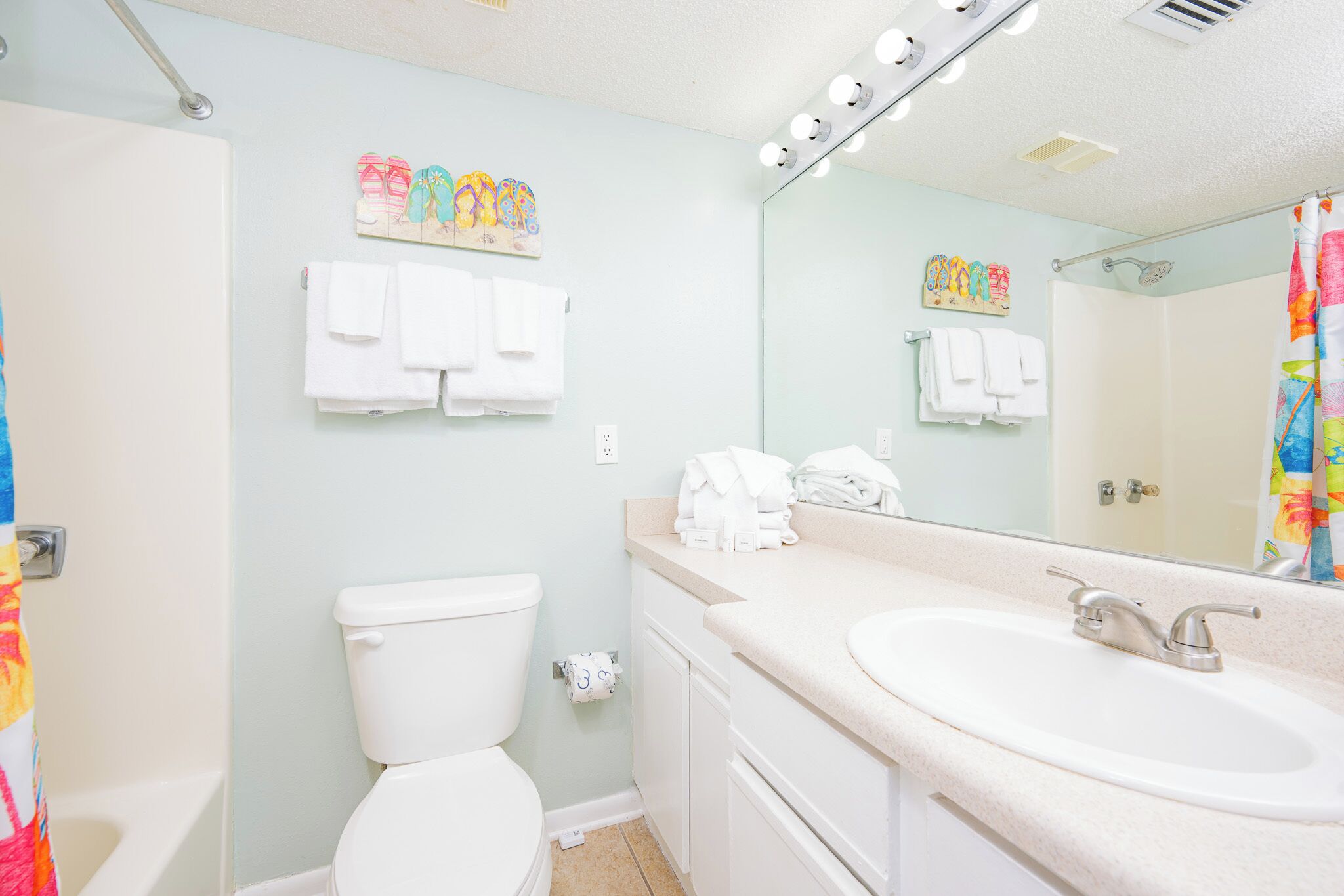 A bathroom with a toilet, sink, and mirror. There are towels hanging on the wall and a shower curtain.
