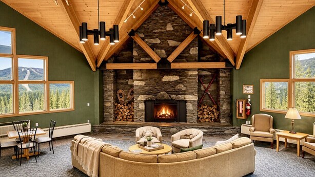Una sala de estar acogedora con chimenea de piedra, vigas de madera y ventanas amplias con vistas al exterior.