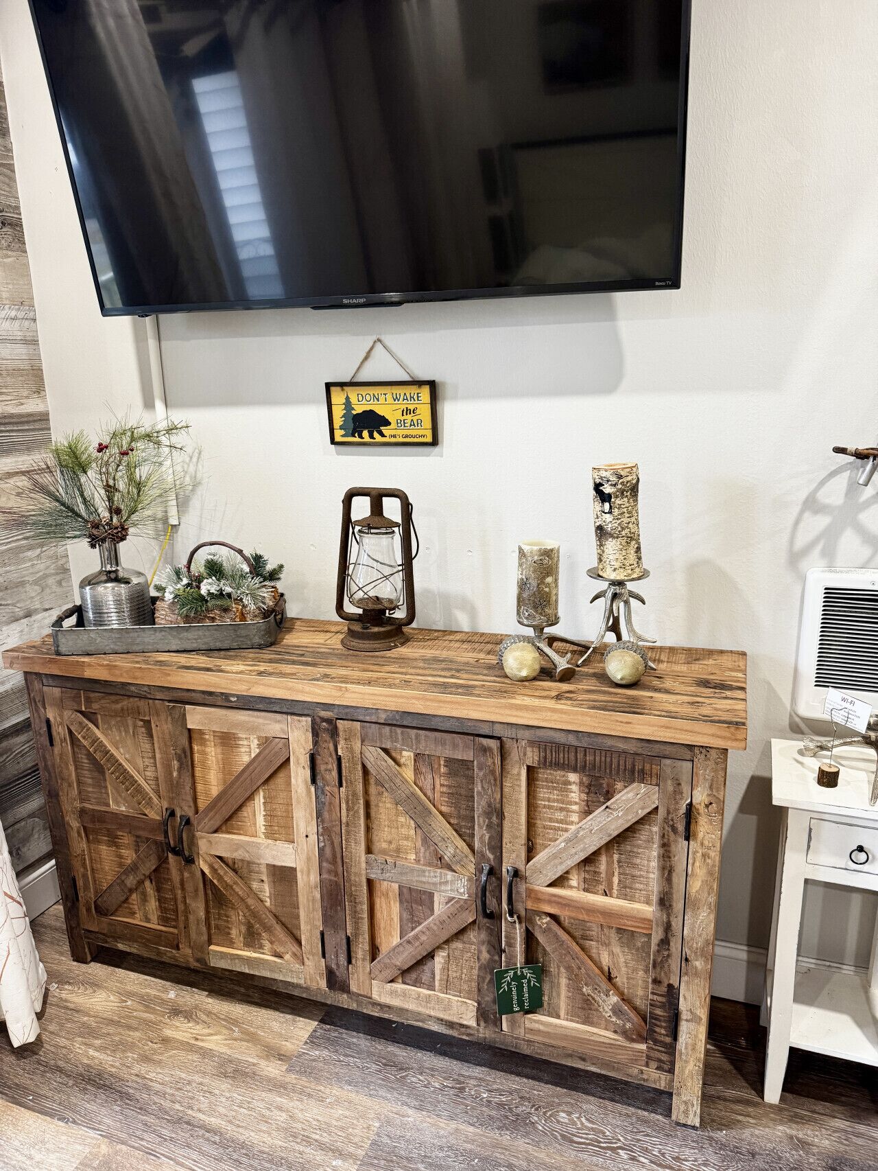 Een rustieke houten console met een tv, decoratieve objecten en een bord erboven.