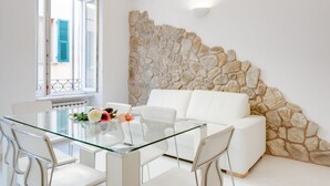 Una sala moderna con una mesa de comedor de cristal, sofá blanco y una pared de acento de piedra.