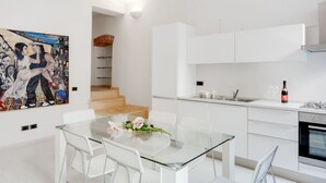 Una cocina moderna con armarios blancos, una mesa de comedor de vidrio y una escalera que sube a un nivel superior.