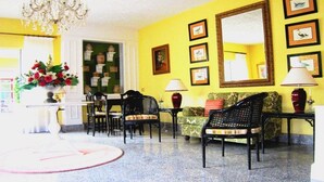 Una habitación con pared amarilla, un candelabro, cuadros enmarcados, un sofá y un comedor con sillas y una mesa.