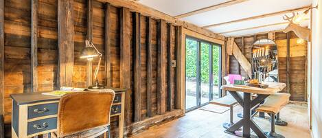 Ein rustikales Holzinterieur mit Schreibtisch, Stuhl und Tisch, und ein Blick ins Freie durch eine Glastür.