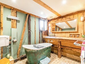 A rustic bathroom with a vintage bathtub, wooden cabinets, and a large mirror.