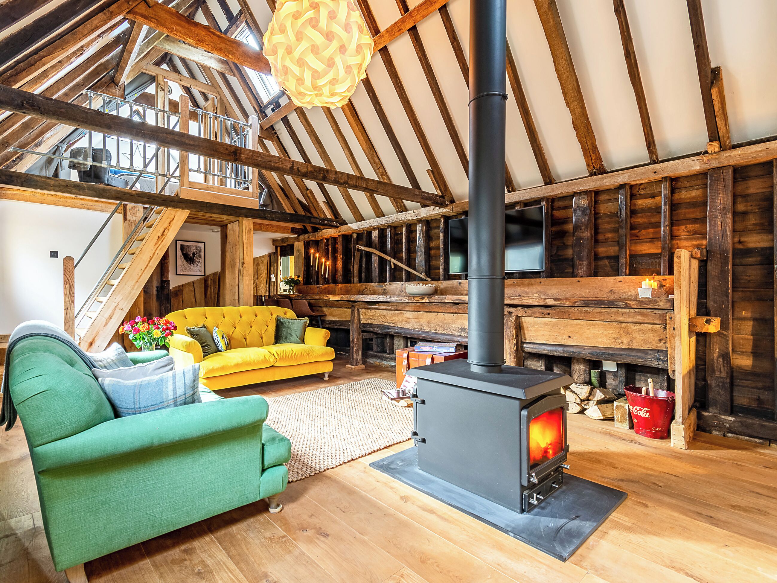 A rustic interior with a wooden ceiling, a sofa, a green armchair, and a wood-burning stove.