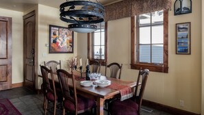 A dining room with a wooden table set for six, surrounded by six chairs with red cushions. There is a chandelier above the table, and a painting on the wall. - Outpost: Grand View 2810 - AC and Close to town! (Jackson)