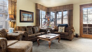 A cozy living room with leather sofas, a wooden coffee table, and large windows offering a view of the outdoors. - Outpost: Grand View 2810 - AC and Close to town! (Jackson)