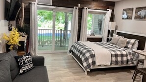 Un dormitorio con cama, sofá, televisión y balcón con vistas a zonas verdes.