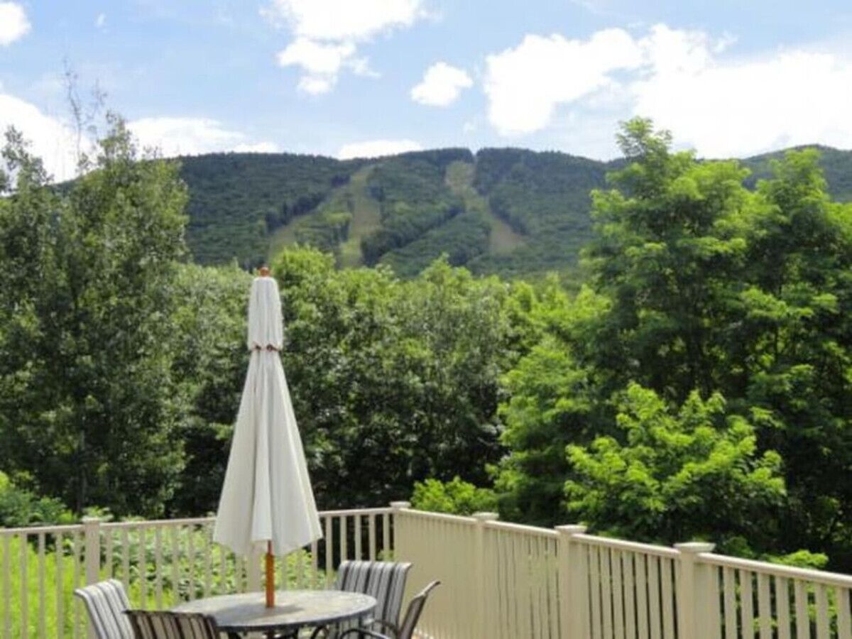 Una terraza con mesa y sillas, rodeada por una valla blanca, con vistas a un paisaje boscoso.