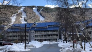 Un hotel con vistas a la montaña, un estacionamiento y terreno cubierto de nieve.