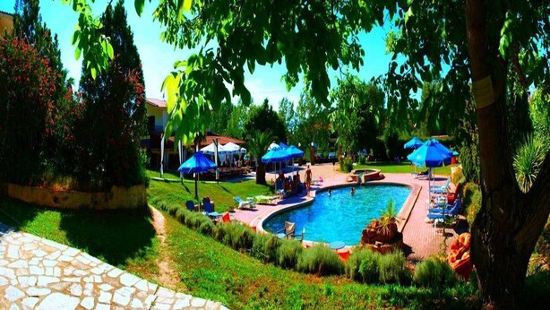 Zona de piscina amb gandules i ombrel·les, envoltada de vegetació i un camí de pedra.