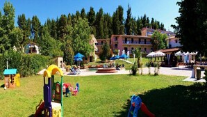 Zona de jocs infantil amb tobogan i estructura per escalar, envoltada per un jardí ben cuidat i un edifici amb balcons al fons.