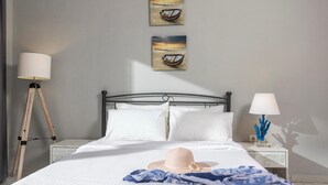 Un llit ben fet amb llençols blancs, una escala de fusta i un teixit blau i blanc estampat. Dues làmpades blanques sobre taulells de nit, i una decoració de corall blau en un d'ells.
