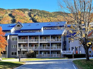 Un edificio a più piani con balconi, con l'insegna 'The Lodge Condominium Hotel', sullo sfondo di alberi e colline dai colori autunnali.