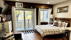 Een slaapkamer met een bed, een bureau, een stoel, een televisie en een raam met gordijnen.
