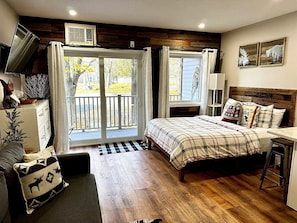 Un dormitorio con cama, escritorio, silla, televisor y ventana con cortinas.