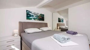 Een moderne slaapkamer met een groot bed, een nachtkastje, een spiegel en een schilderij aan de muur.