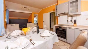 Een eetgedeelte met een tafel voor vier personen, een keuken met moderne apparatuur, en een aparte eetkamer met een groot raam.
