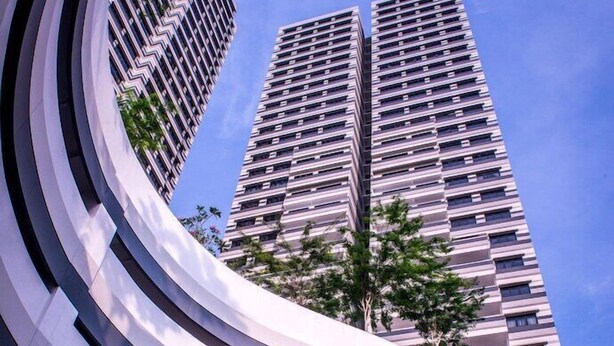 A modern building with a curved facade and a clear view of two tall residential towers in the background. - Ramada by Wyndham Meridin Johor Bahru (Iskandar Puteri)