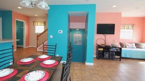 Una sala de estar con televisor, un comedor con mesa lista para cuatro personas y una cocina con microondas.