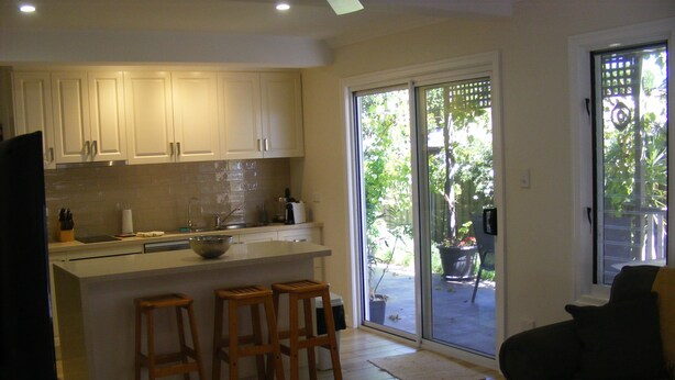 A modern kitchen with white cabinets, a large island with stools, and a sliding glass door leading to a patio.