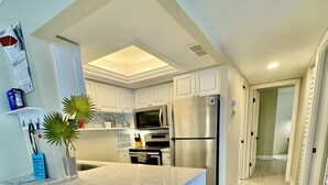 A modern kitchen with white cabinetry, a central island with bar stools, stainless steel appliances, and a calendar on the wall. - Just remodeled, professionally decorated bright and airy! (Siesta Key)