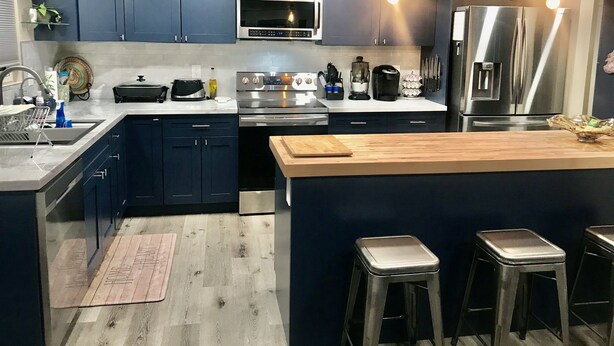 A modern kitchen with dark blue cabinets, stainless steel appliances, a central island with stools, and a skylight above.