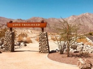 Placa com a inscrição 'COVE TRAILHEAD' na entrada de uma paisagem desértica com montanhas ao fundo.