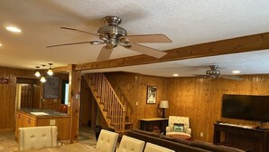 Ein großzügiges Wohnzimmer mit einem Holzespeisetisch und Stühlen, einer Couch, einem Fernseher und einer Treppe, die zu einer anderen Ebene führt.